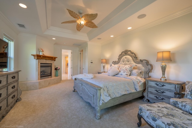 bedroom with ornamental molding, a tray ceiling, light colored carpet, ceiling fan, and a tile fireplace