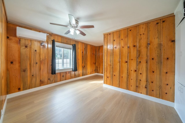 spare room featuring ceiling fan, light wood-type flooring, wooden walls, and a wall unit AC