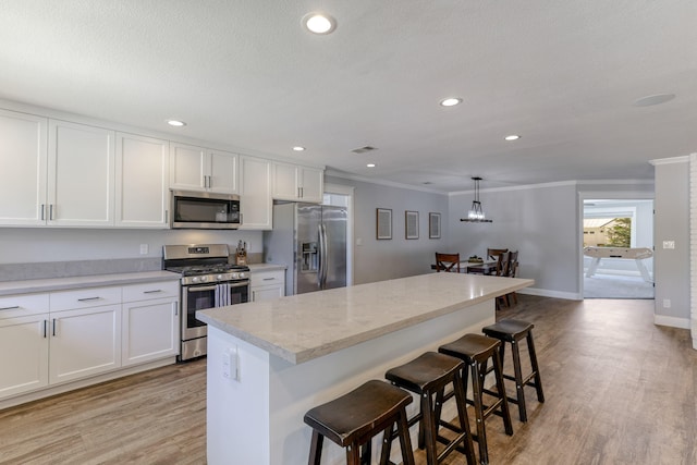 kitchen featuring stainless steel appliances, white cabinetry, a kitchen island, and decorative light fixtures