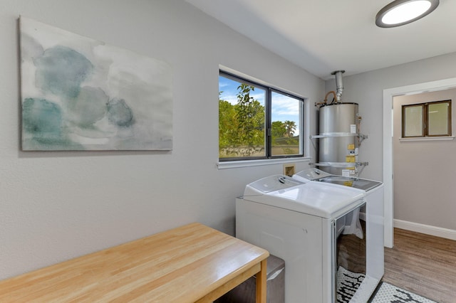 clothes washing area with strapped water heater, independent washer and dryer, and hardwood / wood-style floors