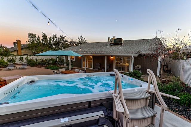 pool at dusk with a patio area and a hot tub