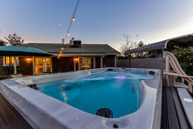 pool at dusk featuring central AC unit and a hot tub