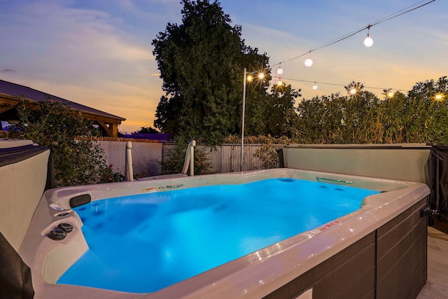 pool at dusk featuring a hot tub