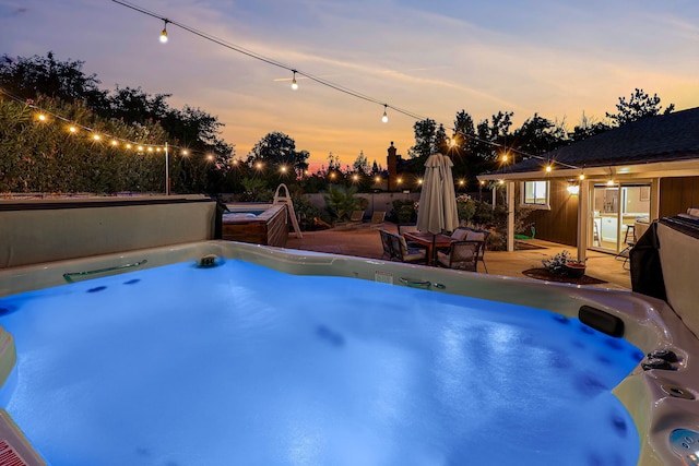 pool at dusk with a hot tub and a patio area