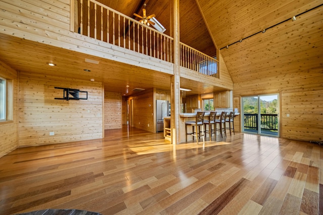 unfurnished living room featuring high vaulted ceiling, ceiling fan, wood walls, and wood ceiling