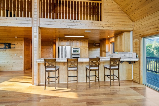 kitchen featuring kitchen peninsula, wooden walls, high vaulted ceiling, and appliances with stainless steel finishes