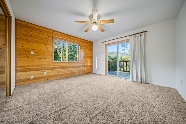 carpeted spare room featuring wood walls and ceiling fan