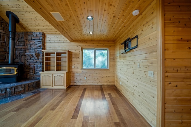 unfurnished living room with light hardwood / wood-style flooring, a wood stove, wood ceiling, and wood walls