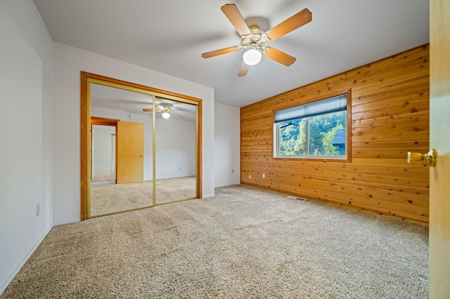 unfurnished bedroom featuring carpet flooring, ceiling fan, and wooden walls