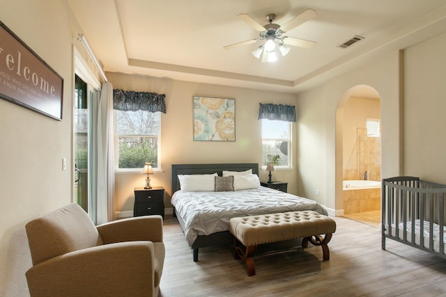 bedroom with hardwood / wood-style floors, ceiling fan, a raised ceiling, and ensuite bathroom