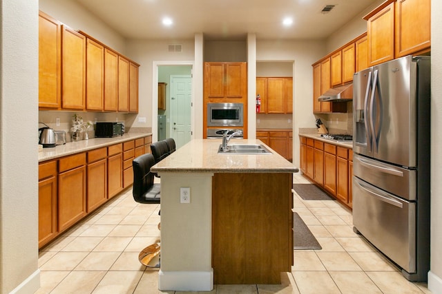 kitchen featuring sink, an island with sink, a breakfast bar area, light tile patterned floors, and appliances with stainless steel finishes