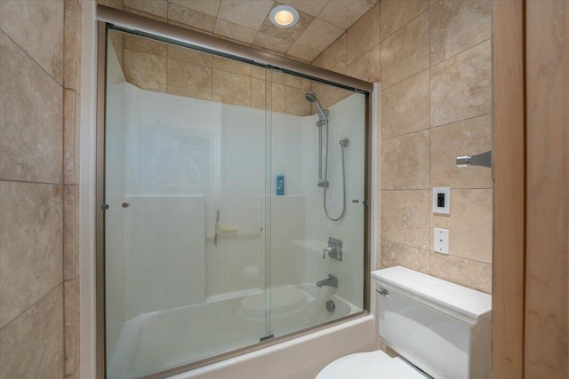 bathroom featuring toilet, shower / bath combination with glass door, and tile walls