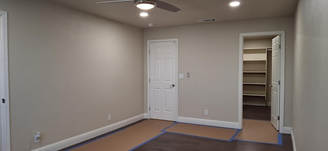 unfurnished bedroom featuring ceiling fan, a walk in closet, a closet, and dark wood-type flooring