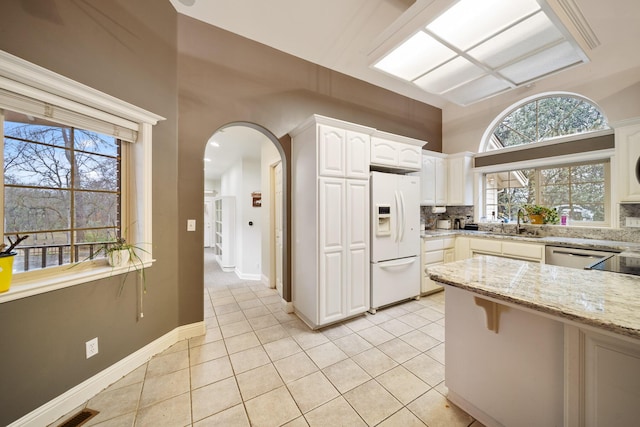 kitchen with white cabinetry, decorative backsplash, white fridge with ice dispenser, light tile patterned floors, and light stone countertops