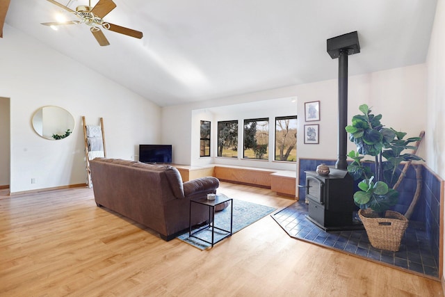 living room featuring lofted ceiling, ceiling fan, light hardwood / wood-style floors, and a wood stove