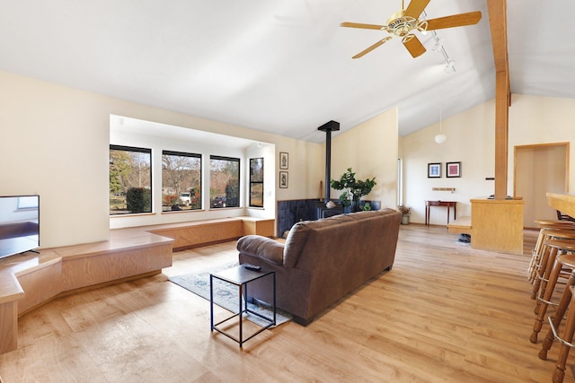 living room featuring ceiling fan, a wood stove, light wood-type flooring, track lighting, and vaulted ceiling with beams