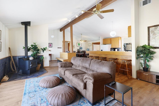 living room featuring ceiling fan, light hardwood / wood-style floors, lofted ceiling with beams, track lighting, and a wood stove