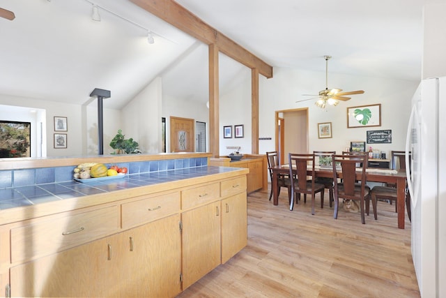 kitchen with white fridge, lofted ceiling with beams, light wood-type flooring, a wood stove, and tile counters