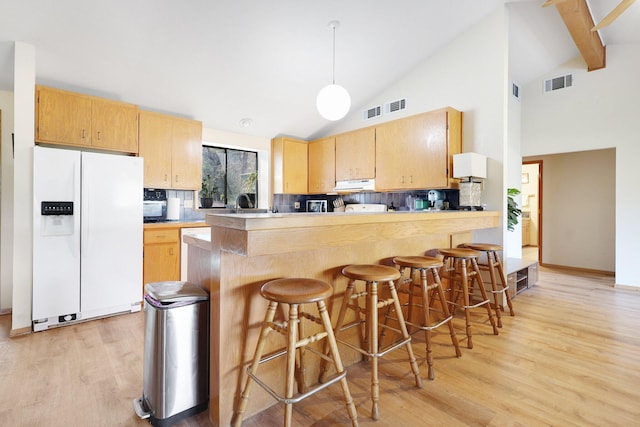 kitchen featuring light hardwood / wood-style floors, backsplash, light brown cabinetry, white fridge with ice dispenser, and beam ceiling