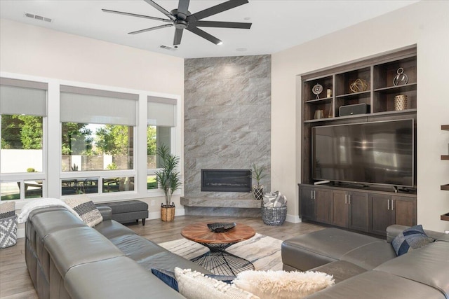 living room with ceiling fan, a high end fireplace, and light hardwood / wood-style flooring