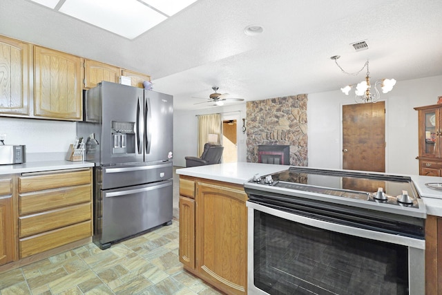 kitchen featuring pendant lighting, ceiling fan, stainless steel appliances, a fireplace, and a textured ceiling