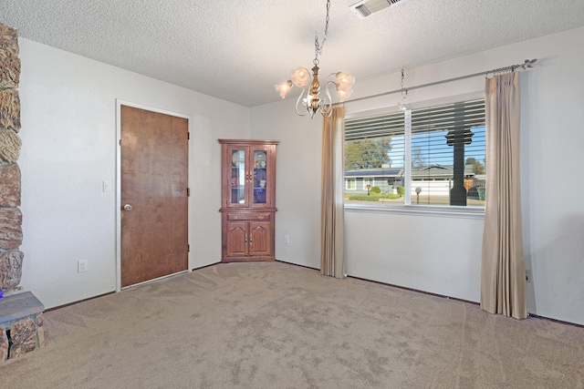 carpeted empty room with a notable chandelier and a textured ceiling