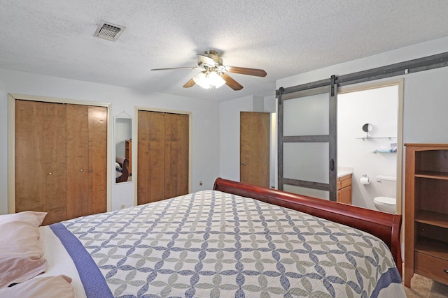 bedroom featuring multiple closets, ensuite bathroom, a barn door, and a textured ceiling