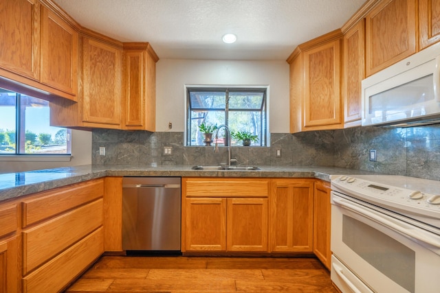 kitchen with tasteful backsplash, sink, white appliances, light wood-type flooring, and a textured ceiling