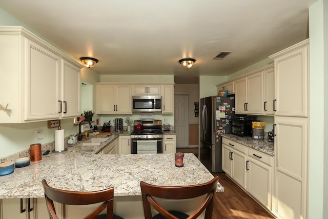 kitchen with kitchen peninsula, stainless steel appliances, a kitchen bar, and sink