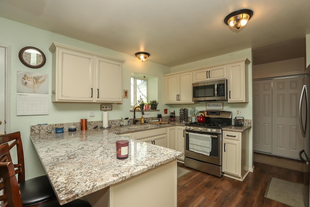 kitchen with light stone counters, kitchen peninsula, stainless steel appliances, dark hardwood / wood-style flooring, and sink