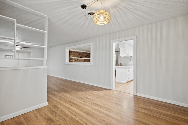 empty room featuring ceiling fan with notable chandelier, a textured ceiling, and light wood-type flooring