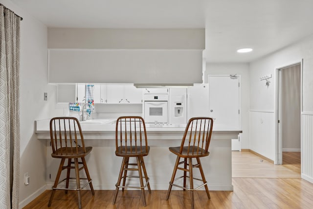 kitchen featuring sink, a kitchen breakfast bar, white appliances, and white cabinets