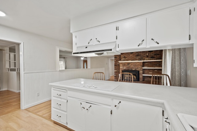 kitchen featuring white cabinets, white electric stovetop, light hardwood / wood-style floors, and a fireplace