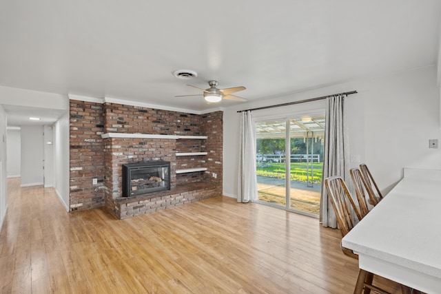 unfurnished living room featuring a brick fireplace, light wood-type flooring, and ceiling fan