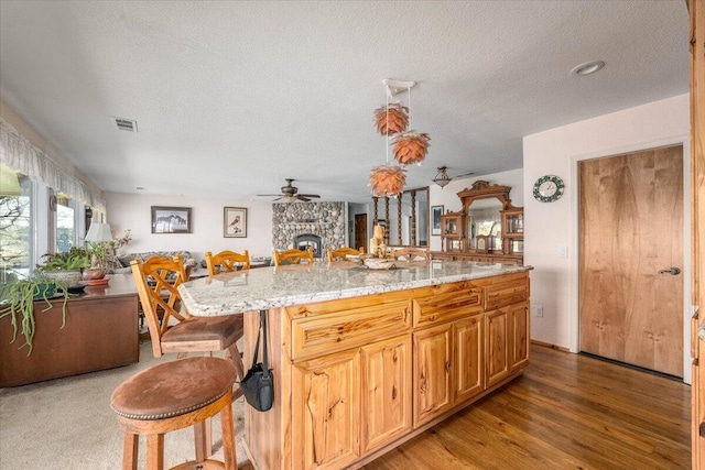 kitchen featuring hardwood / wood-style floors, a kitchen island, a stone fireplace, light stone counters, and a breakfast bar