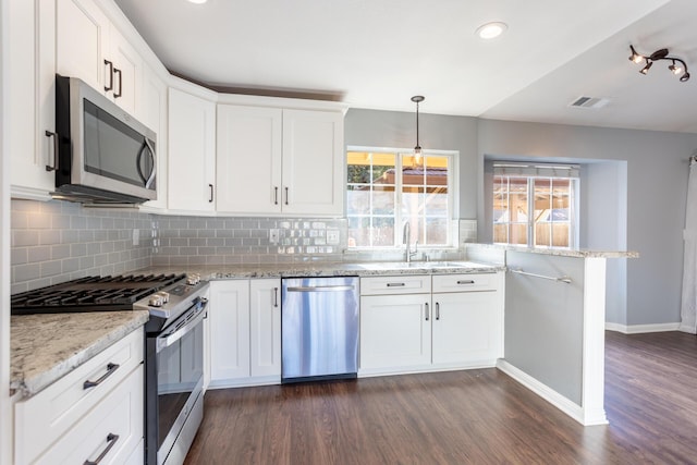 kitchen featuring white cabinetry, hanging light fixtures, appliances with stainless steel finishes, dark hardwood / wood-style flooring, and light stone counters