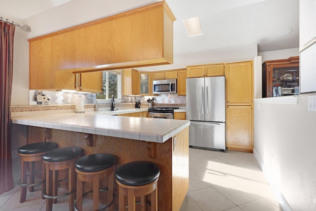 kitchen featuring tasteful backsplash, kitchen peninsula, tile counters, a breakfast bar, and appliances with stainless steel finishes