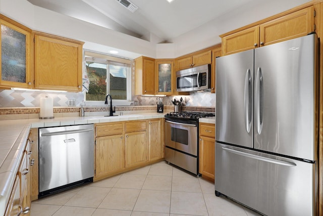 kitchen with tile counters, appliances with stainless steel finishes, sink, lofted ceiling, and tasteful backsplash