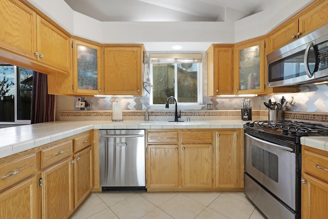 kitchen featuring stainless steel appliances, light tile patterned floors, tile countertops, decorative backsplash, and sink