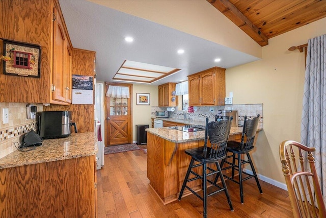 kitchen with a kitchen breakfast bar, decorative backsplash, light hardwood / wood-style floors, and kitchen peninsula