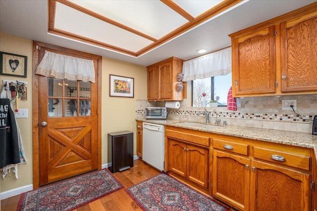 kitchen with light wood-type flooring, white dishwasher, tasteful backsplash, and sink