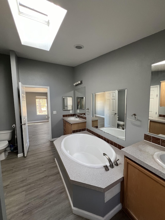 bathroom featuring toilet, a skylight, hardwood / wood-style flooring, a bath, and vanity