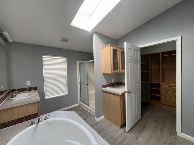 bathroom with vaulted ceiling with skylight, wood-type flooring, separate shower and tub, and vanity