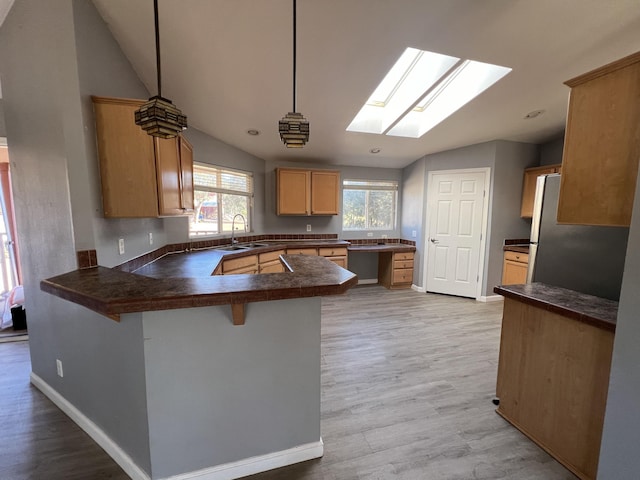 kitchen with a kitchen bar, kitchen peninsula, decorative light fixtures, light wood-type flooring, and sink