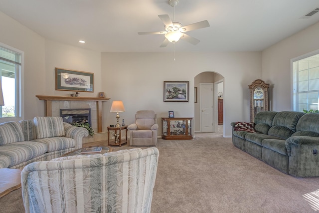 living room with a tiled fireplace, light colored carpet, and ceiling fan