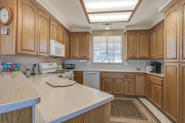 kitchen with sink, light tile patterned floors, kitchen peninsula, light stone countertops, and white appliances