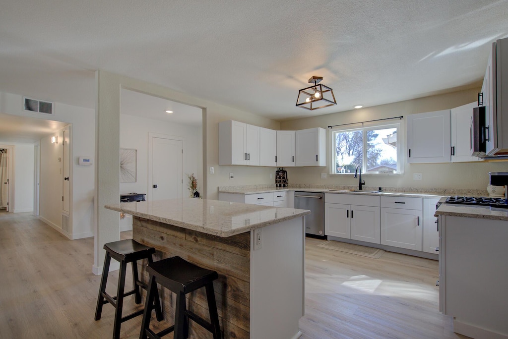 kitchen featuring appliances with stainless steel finishes, white cabinetry, light stone countertops, a kitchen bar, and a center island