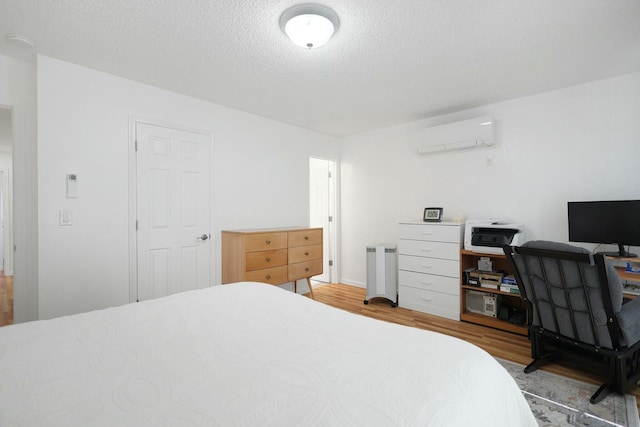 bedroom with a wall mounted air conditioner, a textured ceiling, and light wood-type flooring