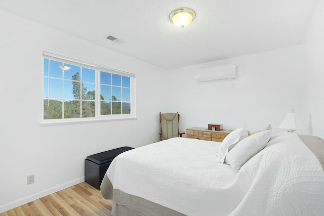 bedroom featuring light wood-type flooring, a textured ceiling, and an AC wall unit