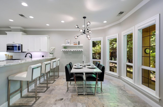 dining space featuring sink, ornamental molding, and a chandelier